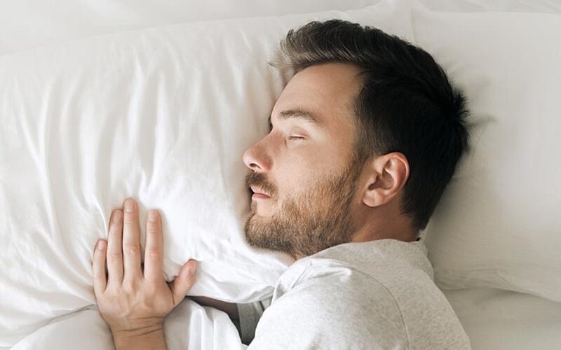 Schlafender Mann in weißem Bett auf der Obersicht. Entspannt, bärtig, bärtig, in einem gemütlichen weißen Schlafzimmer
