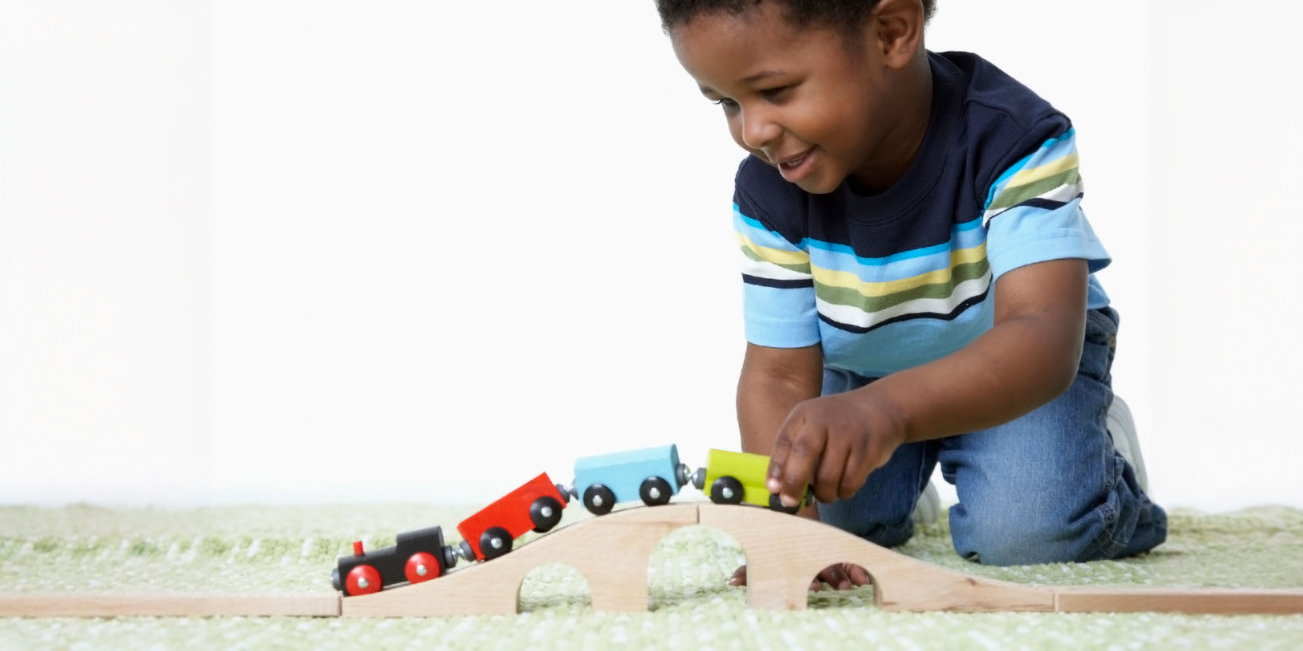 Kleiner Junge spielt fröhlich mit einer Holzeisenbahn.